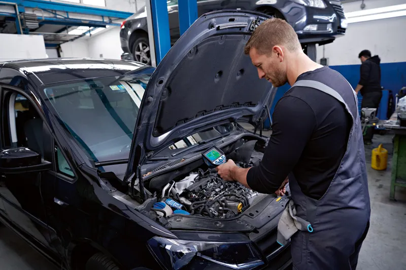 Una persona revisa el motor de un automóvil utilizando una cámara térmica en un taller automotriz.