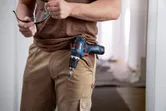 Una persona que sostiene gafas de seguridad con una herramienta combinada inalámbrica sujeta a su bolsillo.