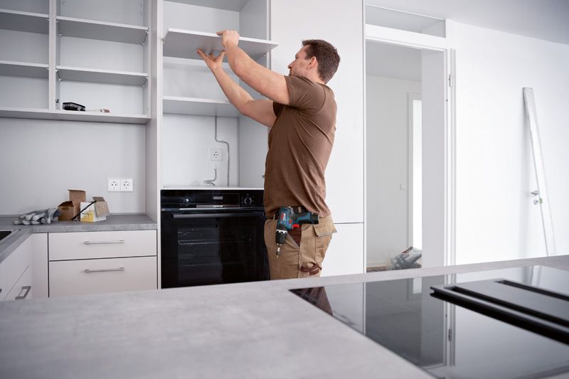 Una persona instala un estante en una cocina, sosteniendo un taladro combinado inalámbrico en su cintura.