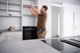 Una persona instala un estante en una cocina, sosteniendo un taladro combinado inalámbrico en su cintura.
