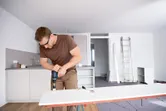 Una persona que usa equipo de seguridad perfora una pizarra blanca en una cocina moderna.