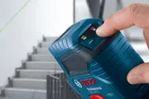 Una persona maneja un nivel láser que proyecta una línea verde cerca de una escalera.