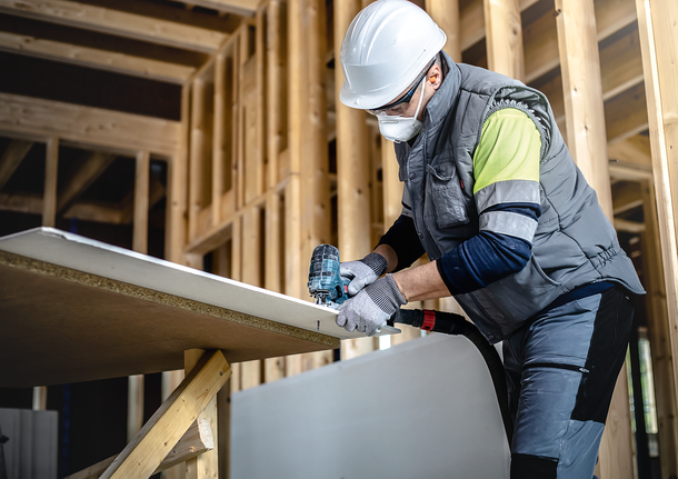 Una persona que lleva equipo de seguridad utiliza una herramienta eléctrica para cortar una tabla de madera.