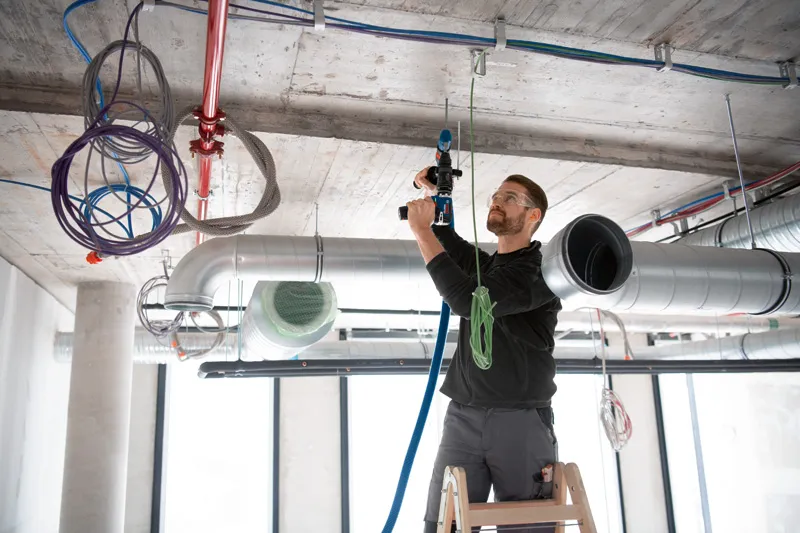 Una persona que usa equipo de seguridad usa un taladro con un adaptador FlexiClick encima de una escalera.