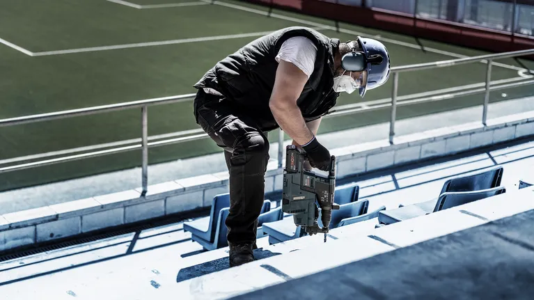 Una persona que usa equipo de seguridad practica ejercicios de percusión en un escalón de hormigón del estadio.