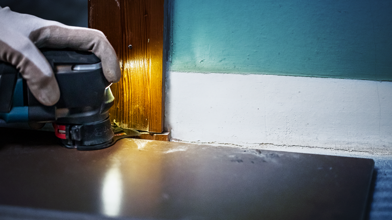 Una persona que usa equipo de seguridad utiliza una herramienta eléctrica para cortar madera cerca de una baldosa del piso.