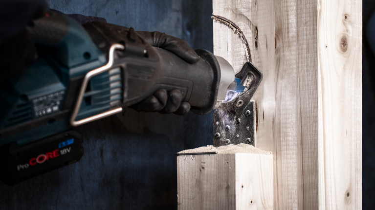 Una persona que lleva puesto un equipo de seguridad utiliza una sierra de vaivén para cortar una viga de madera.