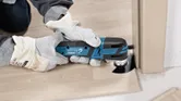Una persona que usa equipo de seguridad corta una tabla de piso de madera con un cortador múltiple inalámbrico.
