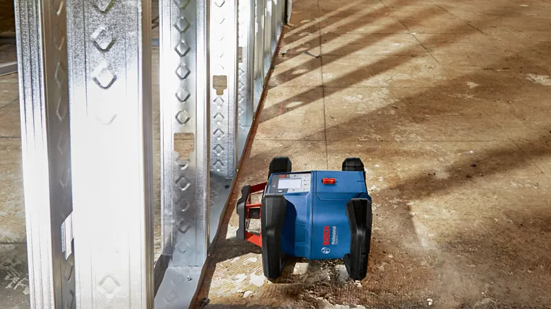 Herramienta de nivelación láser que proyecta pautas junto a marcos de pared de metal en un piso de construcción.