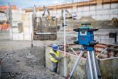 Herramienta de nivelación láser sobre un trípode en un sitio de construcción, persona con equipo de seguridad.