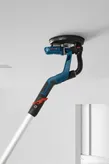 Lijadora de paneles de yeso de cuello largo alisando un techo blanco en una habitación sin terminar.