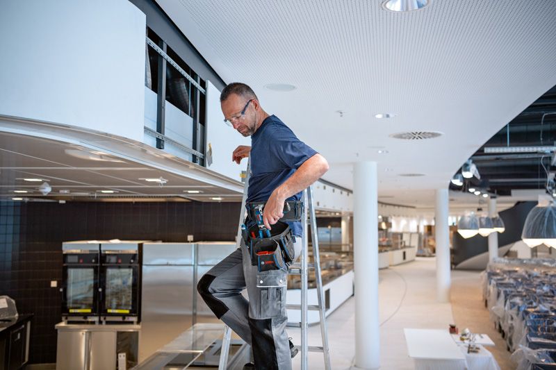 Una persona que usa equipo de seguridad se sube a una escalera instalando un sistema de ventilación.