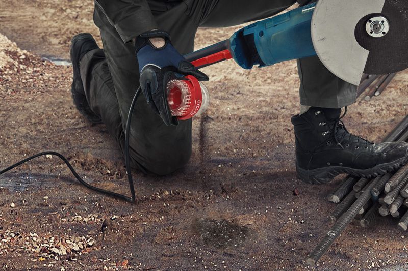 Una persona que usa equipo de seguridad utiliza una amoladora angular para cortar varillas de metal en el suelo.