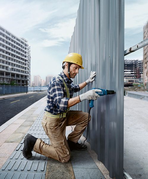 Una persona que usa equipo de seguridad perfora una placa de metal en una obra en construcción.