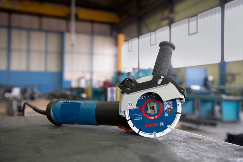 Amoladora angular con sistema X-LOCK apoyada sobre un banco de trabajo en un taller industrial.