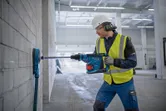 Una persona que usa equipo de seguridad perfora una pared de concreto en un gran espacio interior.