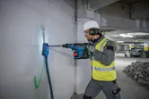 Una persona que usa equipo de seguridad perfora una pared de hormigón con un martillo perforador inalámbrico.