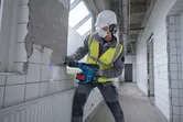 Una persona que usa equipo de seguridad utiliza un martillo rotatorio inalámbrico para romper una pared de azulejos.
