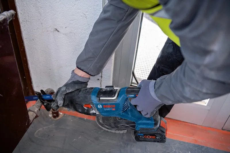 Una persona que usa equipo de seguridad corta metal utilizando una sierra alternativa inalámbrica.