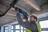 Una persona que usa equipo de seguridad utiliza una sierra alternativa para cortar un tubo que se encuentra en lo alto.