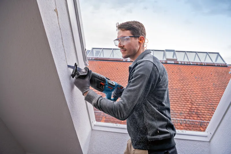 Una persona que usa equipo de seguridad corta una pared con una sierra alternativa.