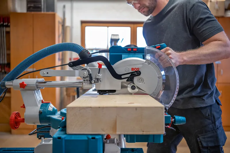 Una persona que usa equipo de seguridad opera una sierra ingletadora para cortar una viga de madera.