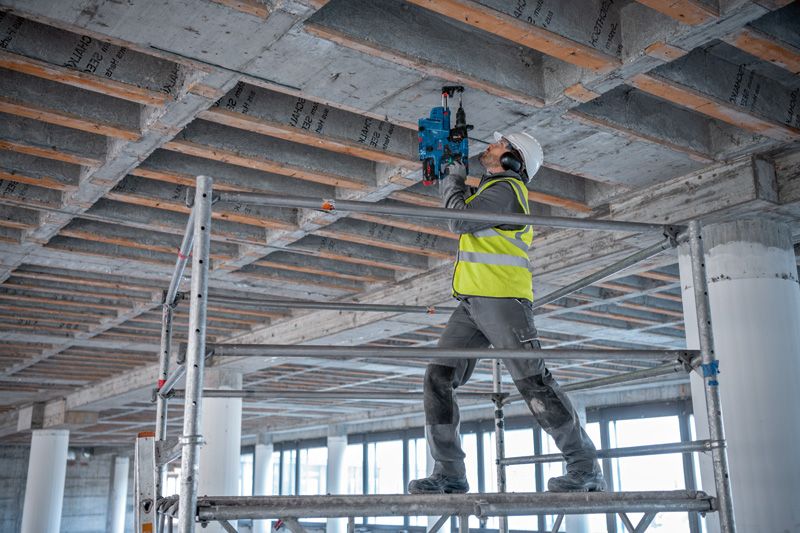 Una persona que usa equipo de seguridad perfora un techo de hormigón en un sitio de construcción.