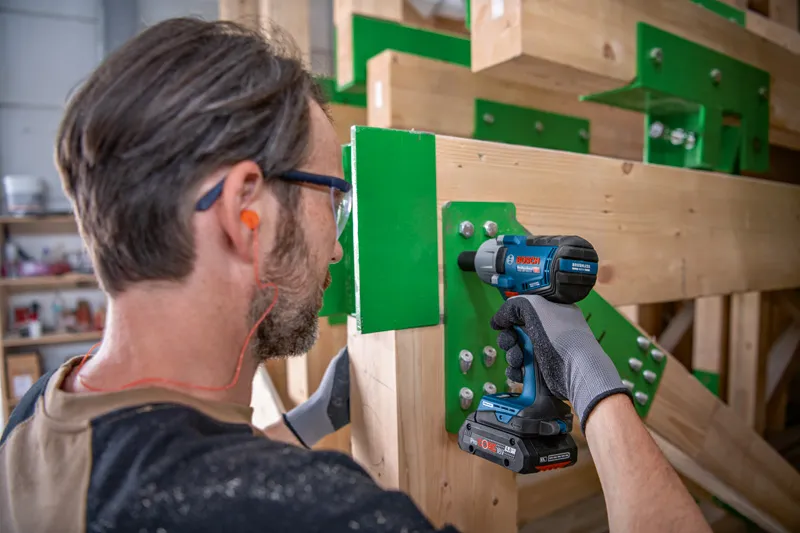 Una persona que usa equipo de seguridad utiliza una llave de impacto para apretar pernos en un marco de madera.