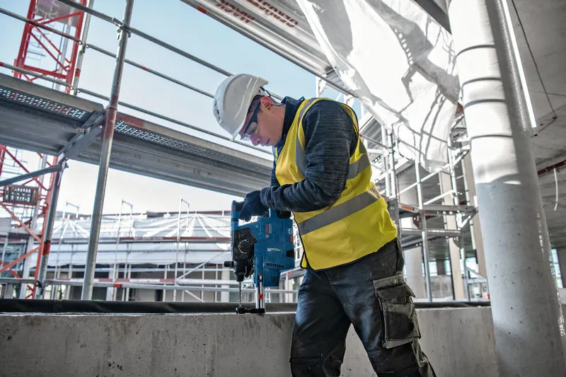 Una persona que usa equipo de seguridad perfora hormigón en un sitio de construcción.
