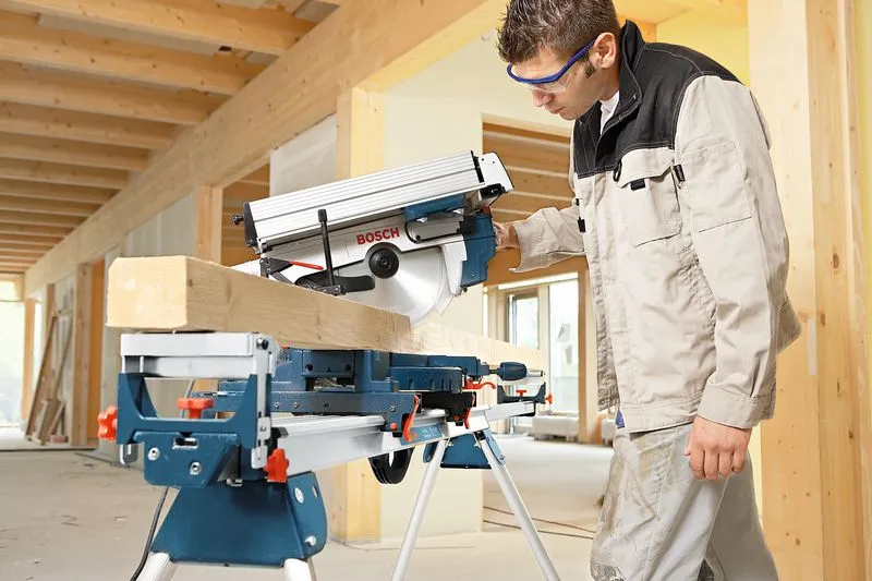 Una persona que usa equipo de seguridad utiliza una sierra ingletadora para cortar una viga de madera en el interior.