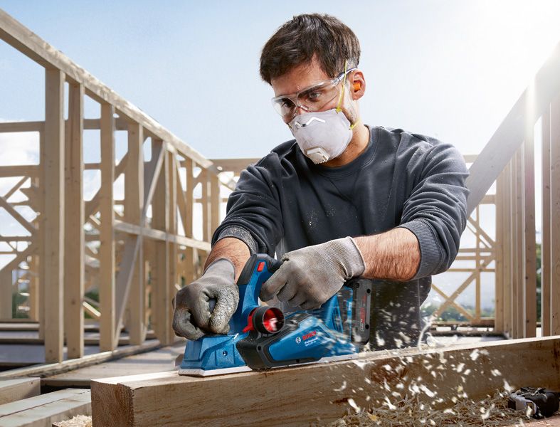Una persona que usa equipo de seguridad cepilla una viga de madera en un sitio de construcción.