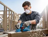 Una persona que usa equipo de seguridad cepilla una viga de madera en un sitio de construcción.