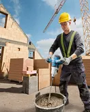 Una persona que usa equipo de seguridad mezcla cemento con un mecanismo de agitación en un sitio de construcción.