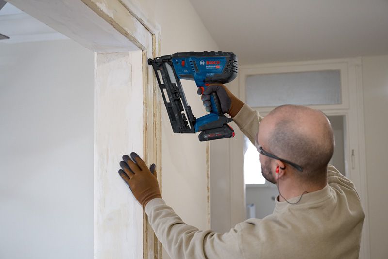 Una persona que usa equipo de seguridad instala molduras de madera utilizando una clavadora inalámbrica.