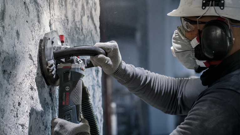 Una persona que usa equipo de seguridad utiliza una amoladora eléctrica para lijar una pared de hormigón.
