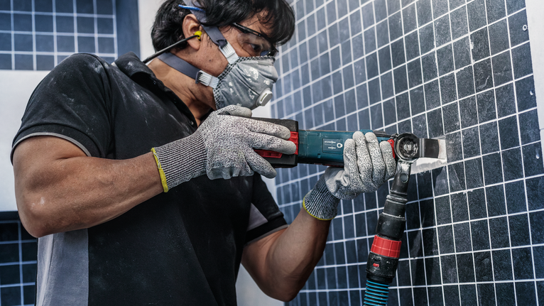 Una persona que usa equipo de seguridad utiliza una herramienta eléctrica para cortar azulejos en una pared.