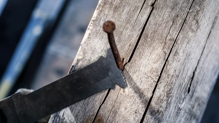 Hoja de sierra alternativa cortando un clavo oxidado incrustado en madera vieja.