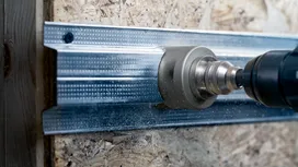 Una herramienta eléctrica con un accesorio de sierra de corona corta un montante metálico.
