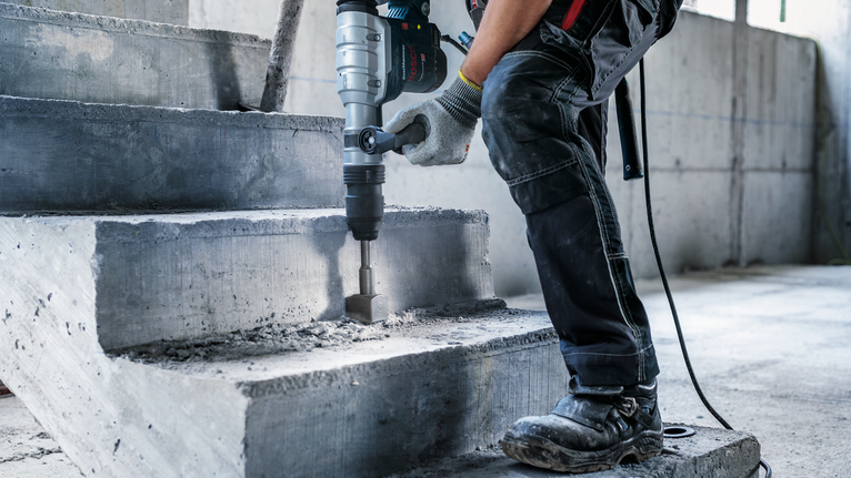 Una persona que usa equipo de seguridad utiliza un martillo rotatorio para romper escaleras de hormigón.