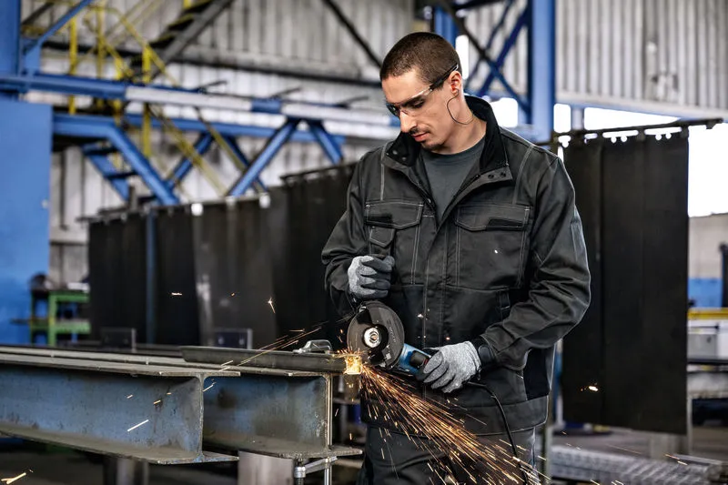 Una persona que usa equipo de seguridad muele metal con una amoladora angular en un taller.