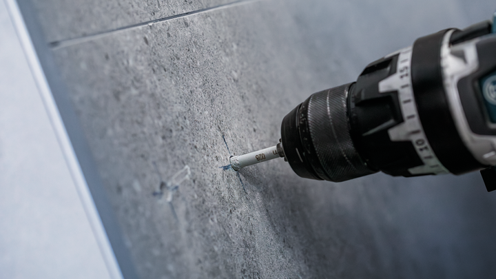 Un taladro que hace un agujero preciso en una pared de azulejos grises.