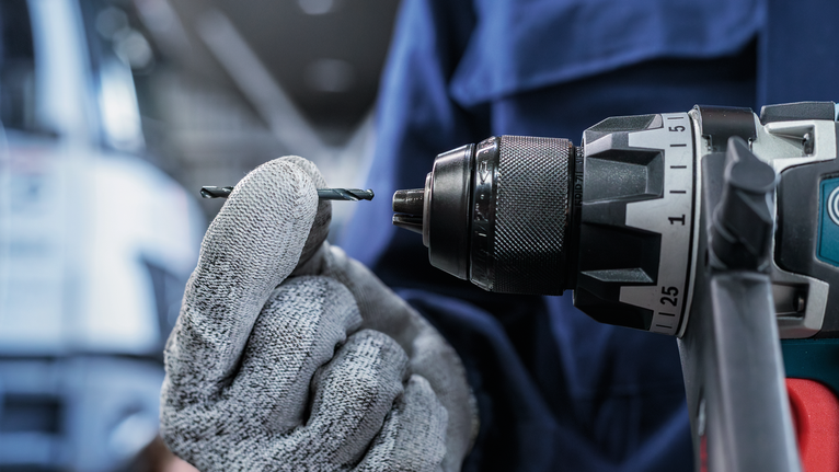 Una persona que usa equipo de seguridad inserta una broca en un taladro eléctrico.