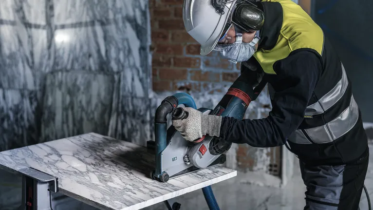 Una persona que usa equipo de seguridad corta una losa de mármol con una sierra circular eléctrica.