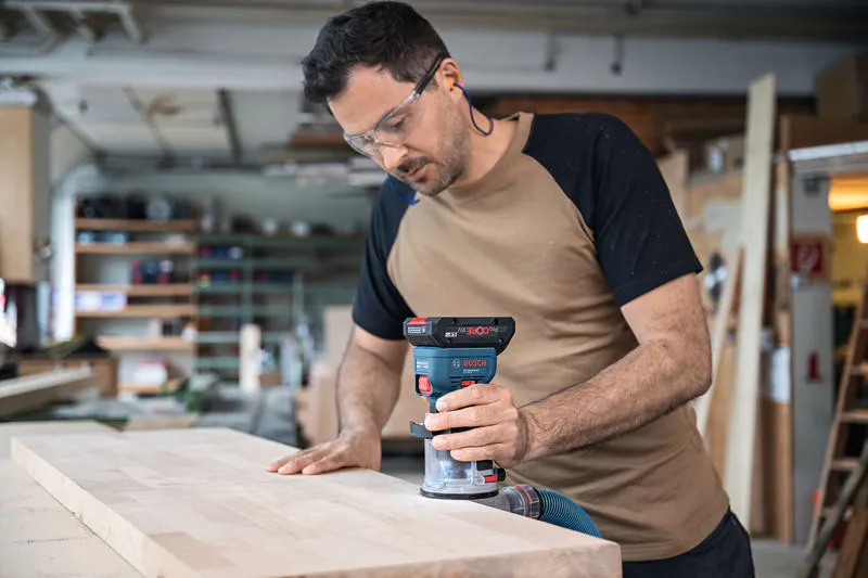Una persona que usa equipo de seguridad fresa el borde de una tabla de madera con una fresadora de palma inalámbrica.