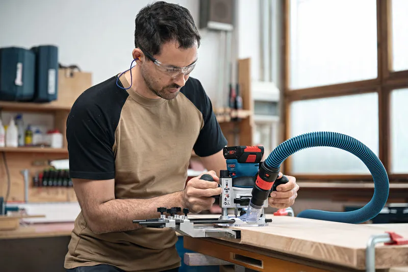 Una persona que usa equipo de seguridad opera una fresadora de palma inalámbrica sobre una tabla de madera.