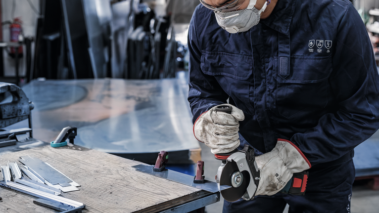 Una persona que usa equipo de seguridad utiliza una amoladora para cortar láminas de metal.