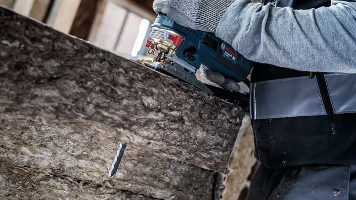 Una persona que usa equipo de seguridad corta material aislante con una sierra de calar.