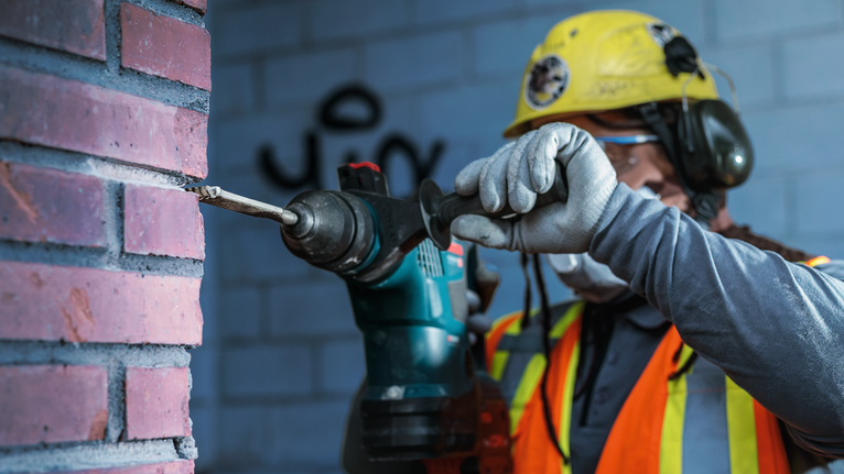 Una persona que lleva equipo de seguridad perfora una pared de ladrillos.