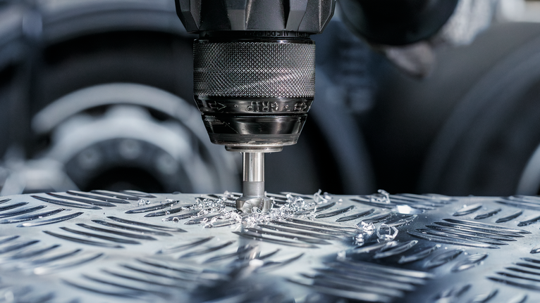 Taladro que realiza un agujero en una placa de metal con virutas de metal alrededor de la broca.