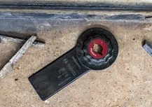 Hoja de herramienta oscilante para cortar plásticos apoyados sobre una superficie de hormigón.